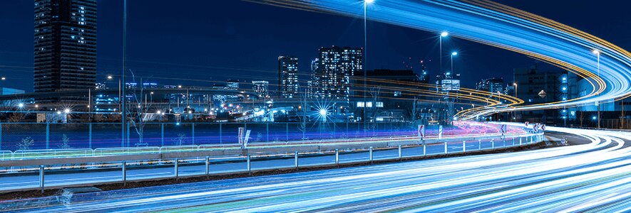 Langzeitbelichtungsaufnahme einer Straße mit blau leuchtenden Lichtspuren, die Geschwindigkeit und Datenfluss symbolisieren.