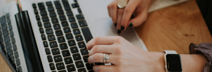 Eine Frau mit mehreren Ringen an der Hand tippt auf ihrem Laptop.