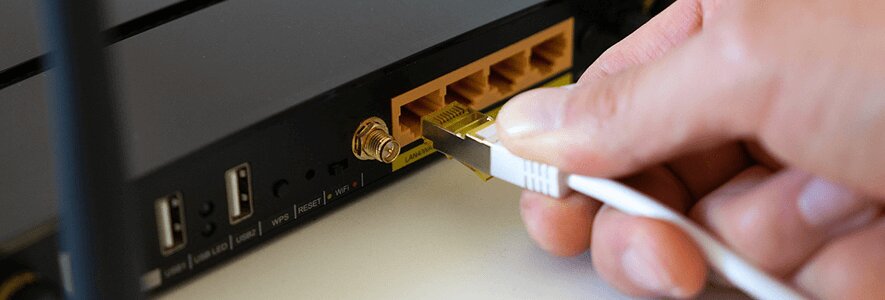 Eine Hand steckt ein weißes Ethernet-Kabel in den LAN-Port eines schwarzen Routers mit goldenen Anschlüssen.