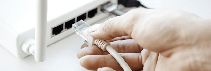 Eine Hand steckt ein weißes Ethernet-Kabel in den Anschluss eines weißen WLAN-Routers mit Antenne.