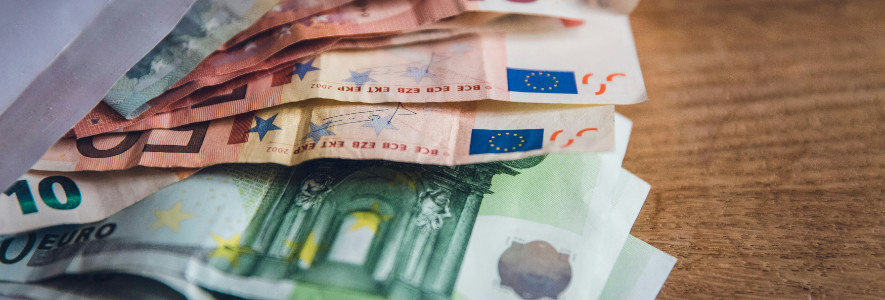 Mehrere Euro-Scheine in unterschiedlichen Farben liegen leicht gefächert auf einem Holztisch.