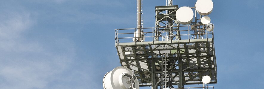 Ein großer Mobilfunkmast mit mehreren Antennen und Parabolspiegeln vor blauem Himmel.