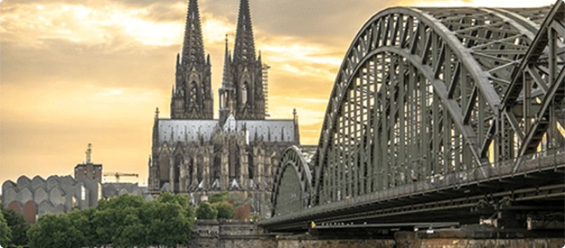 Blick auf den Kölner Dom mit der Hohenzollernbrücke über den Rhein bei Sonnenuntergang.